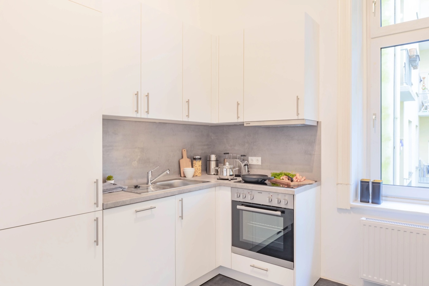 Weiße L-Küche von ROOMHERO in Hamburg, ausgestattet mit Geräten, Geschirr und Kochutensilien